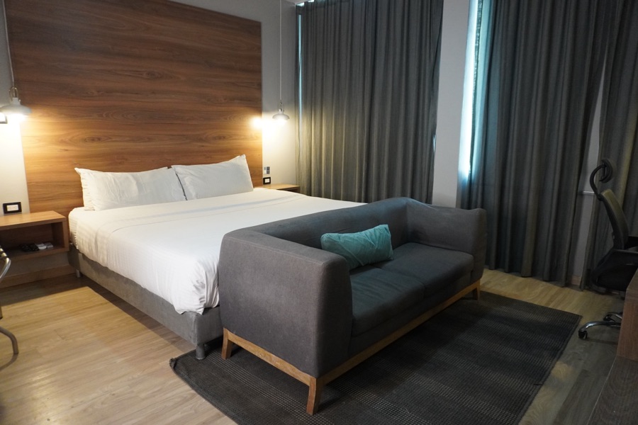 Premium room with a king bed, grey sofa and a large curtained window